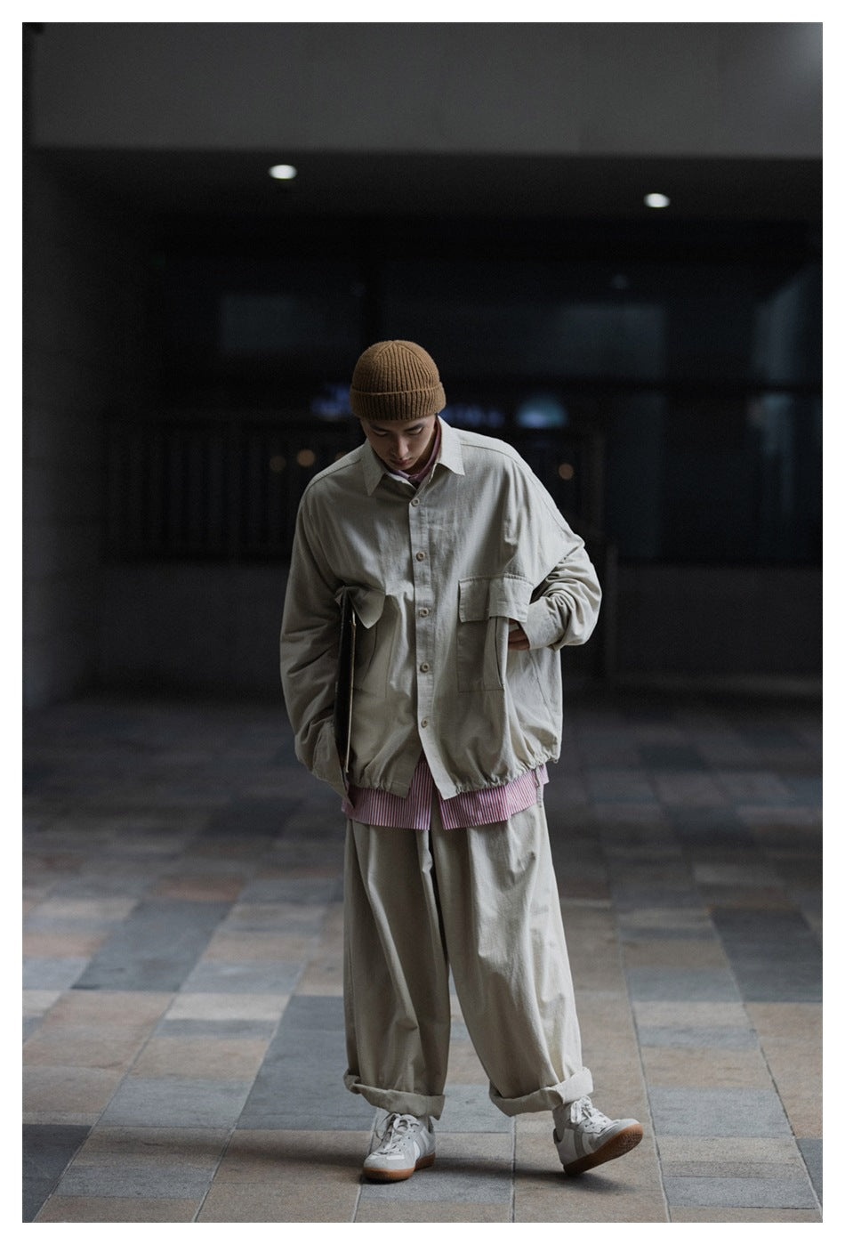 Model wearing an oversized light khaki button-front shirt jacket with a large chest pocket and loose trousers.