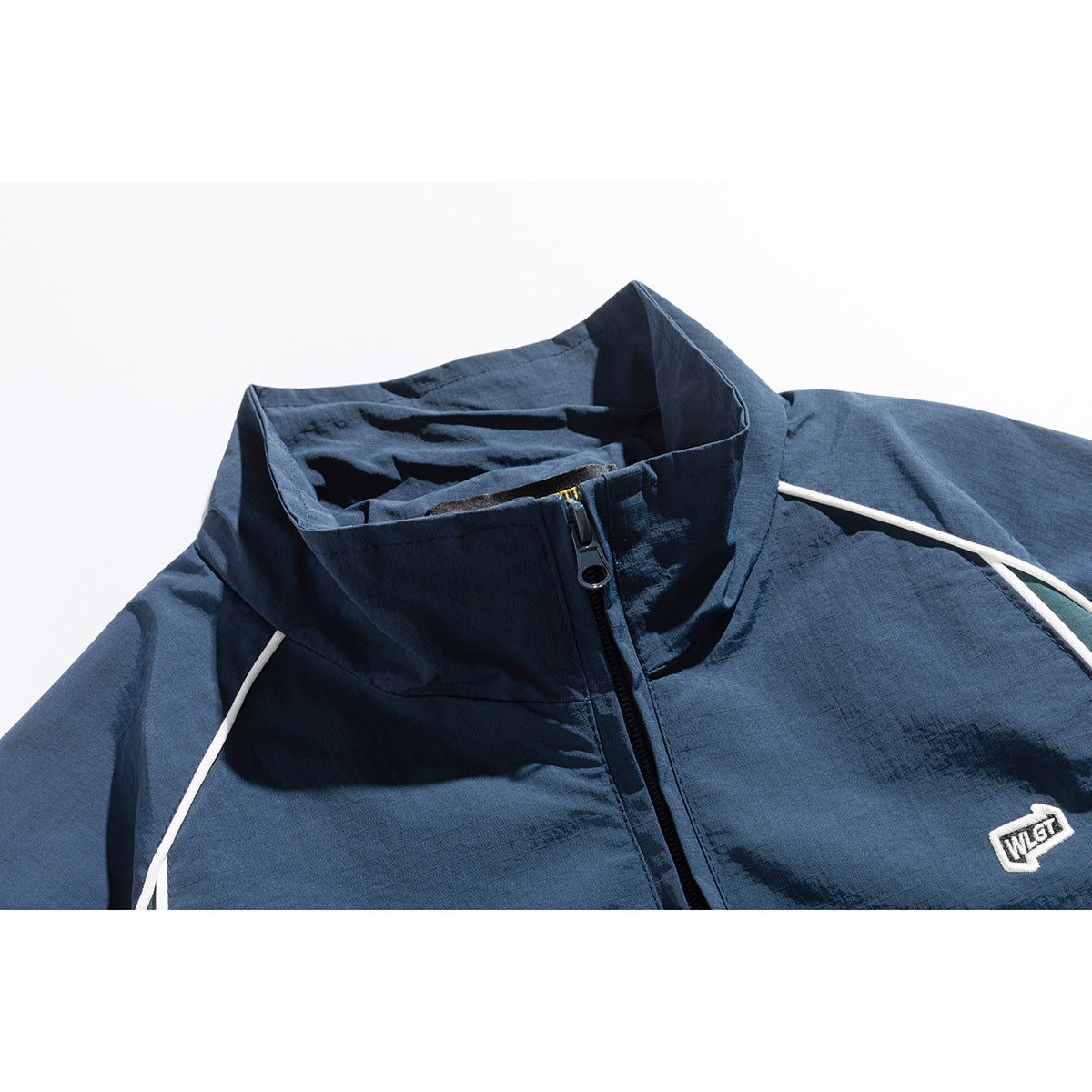 Close-up of a navy zip-up jacket with a tall collar, white piping and a small embroidered chest patch.