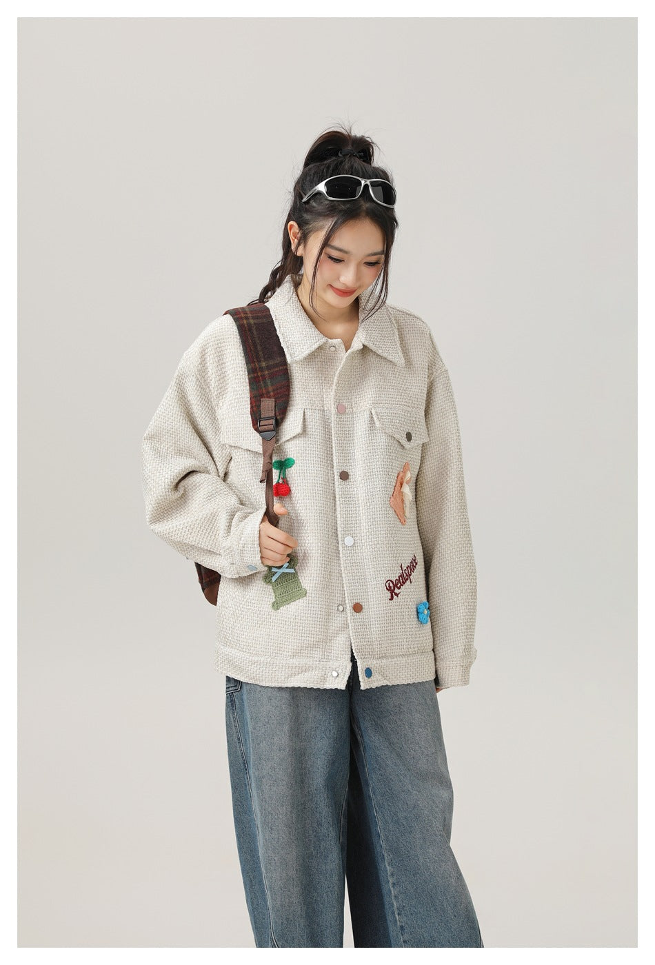 Model in the light khaki textured jacket with crochet appliqués, a plaid backpack strap and wide-leg jeans