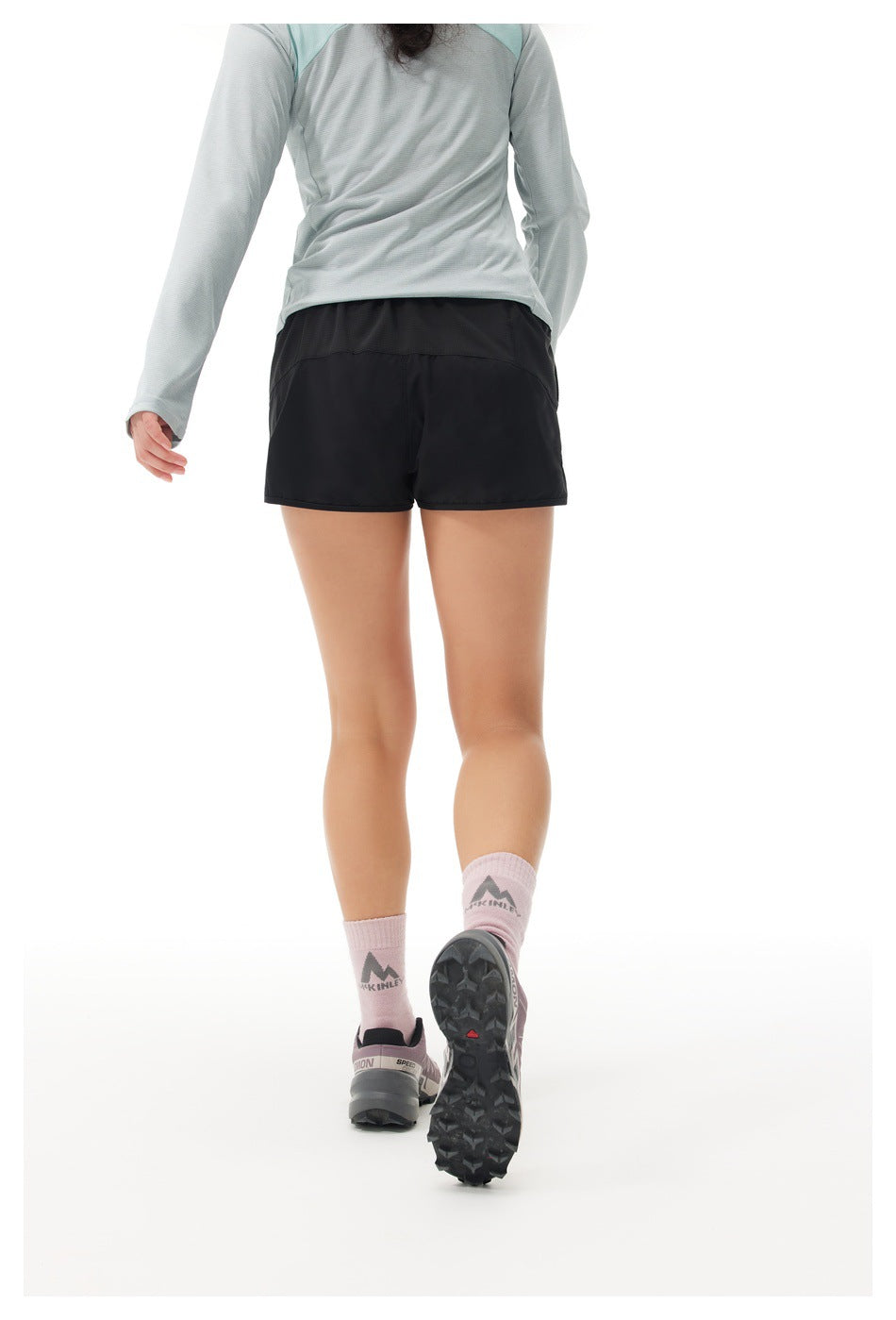 Back view of a model wearing black running shorts with a wide waistband and a light gray long-sleeve top.