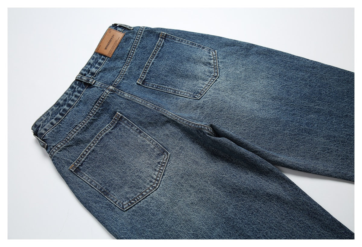 Flat-lay rear view of blue jeans showing two back pockets, waistband, belt loops and a tan leather patch.