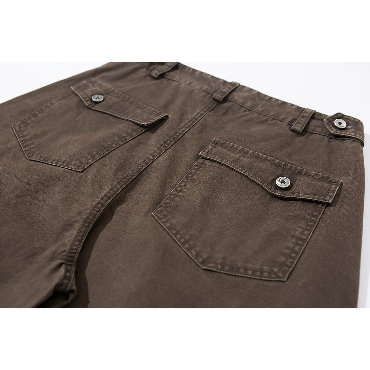 Close-up of the back of brown trousers with two button-flap pockets and belt loops.