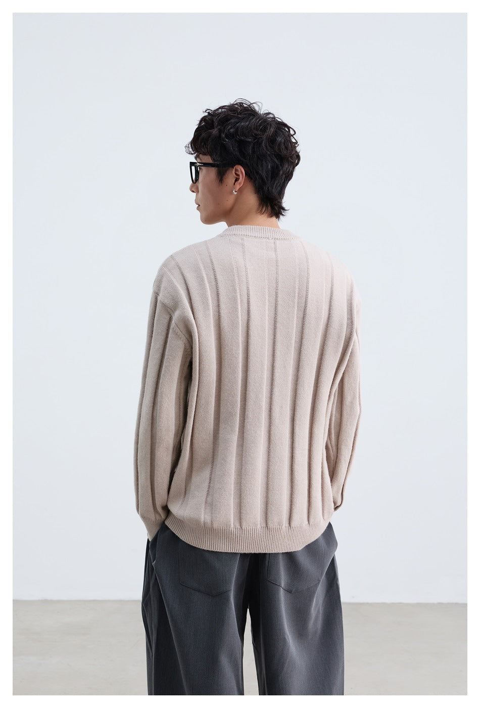 Back view of a model wearing a pale beige ribbed sweater with a ribbed crew neck and hem.