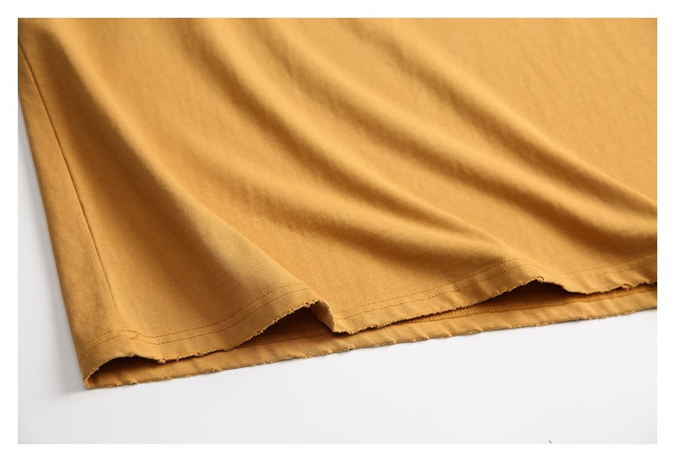 Close-up of the mustard-gold shirt's bottom hem, showing stitching and a slightly uneven edge.