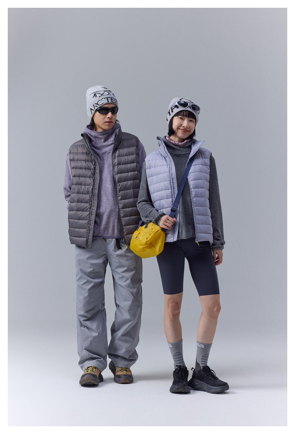 Two models show charcoal and pale lavender quilted puffer vests, layered over fleece tops.