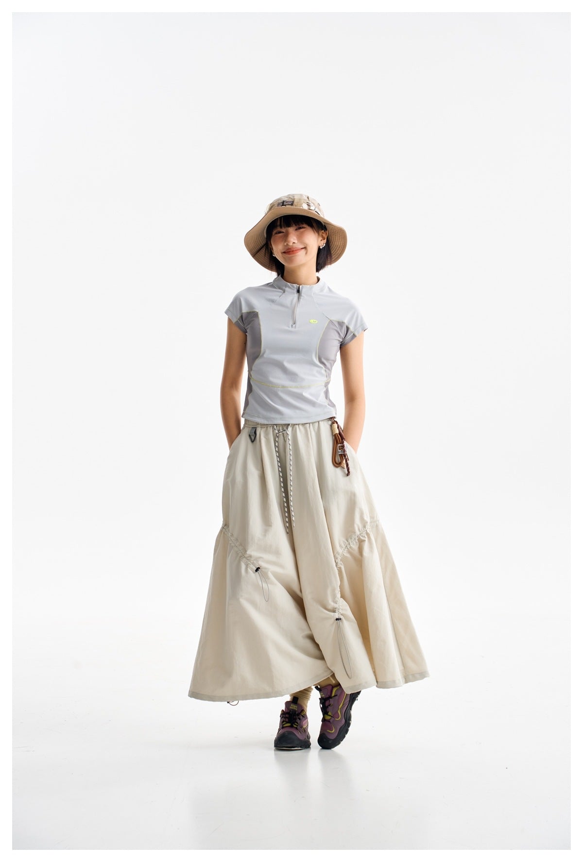 Model wearing a pale gray cap-sleeve quarter-zip top with darker panels and a long cream skirt.