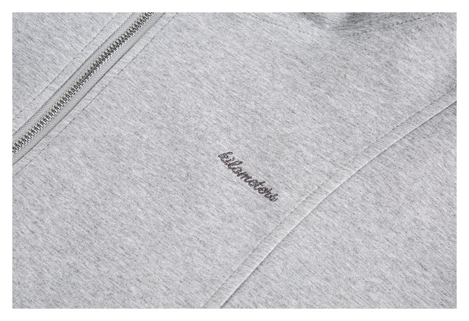 Close-up of cursive embroidery on a light gray sweatshirt beside part of its silver zipper.