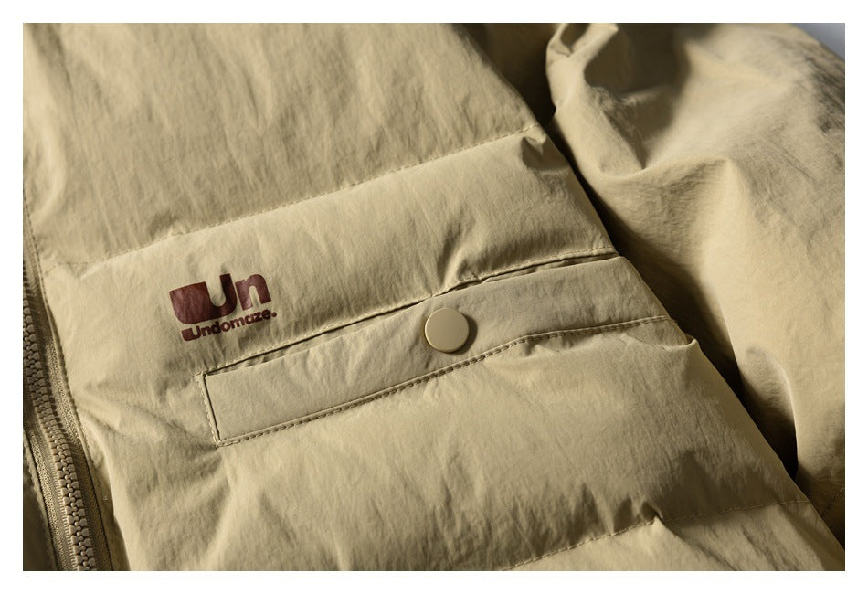 Close-up of a khaki jacket chest pocket with a snap tab and dark red garment logo.