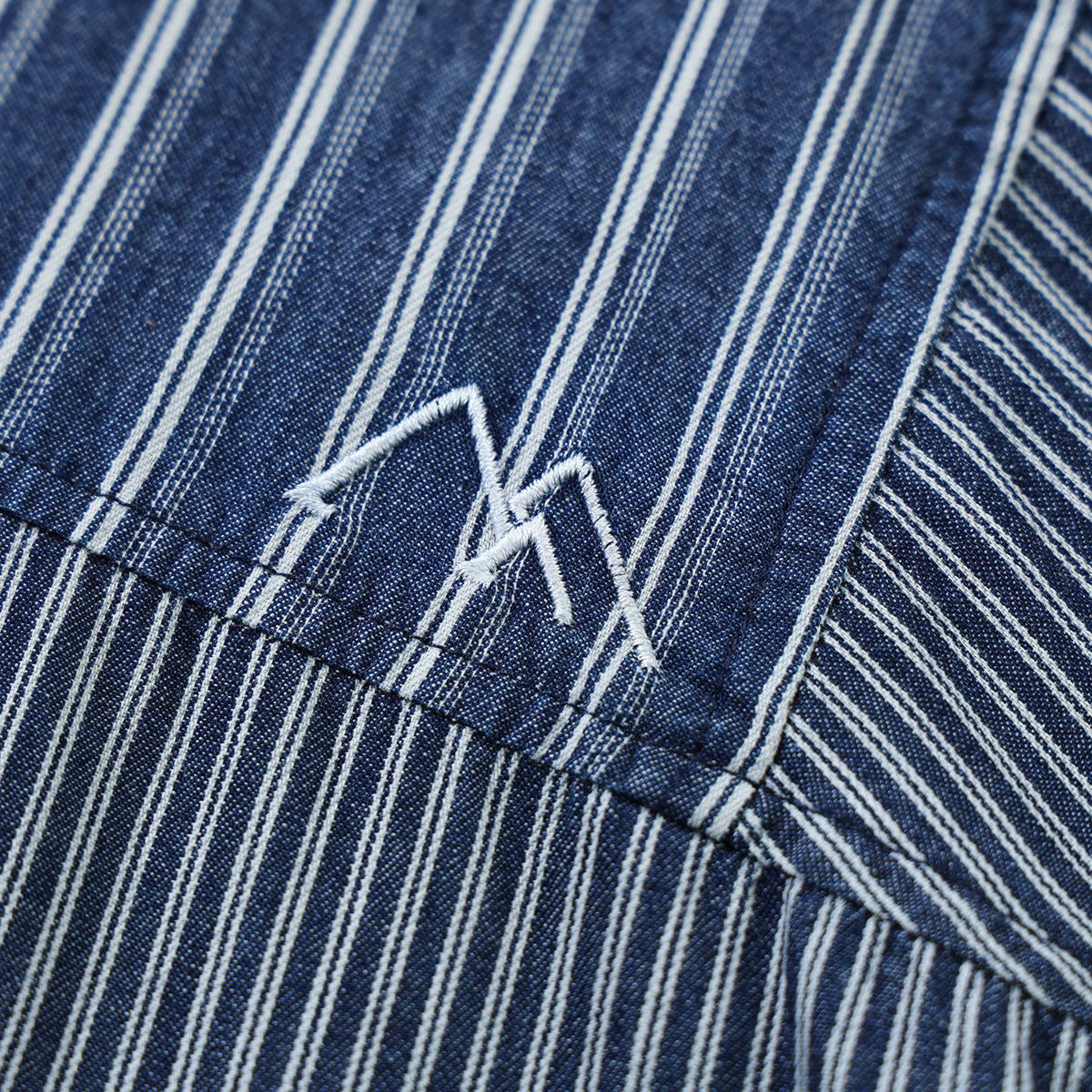 Close-up of a white angular embroidered mark on blue-and-white striped shirt fabric.