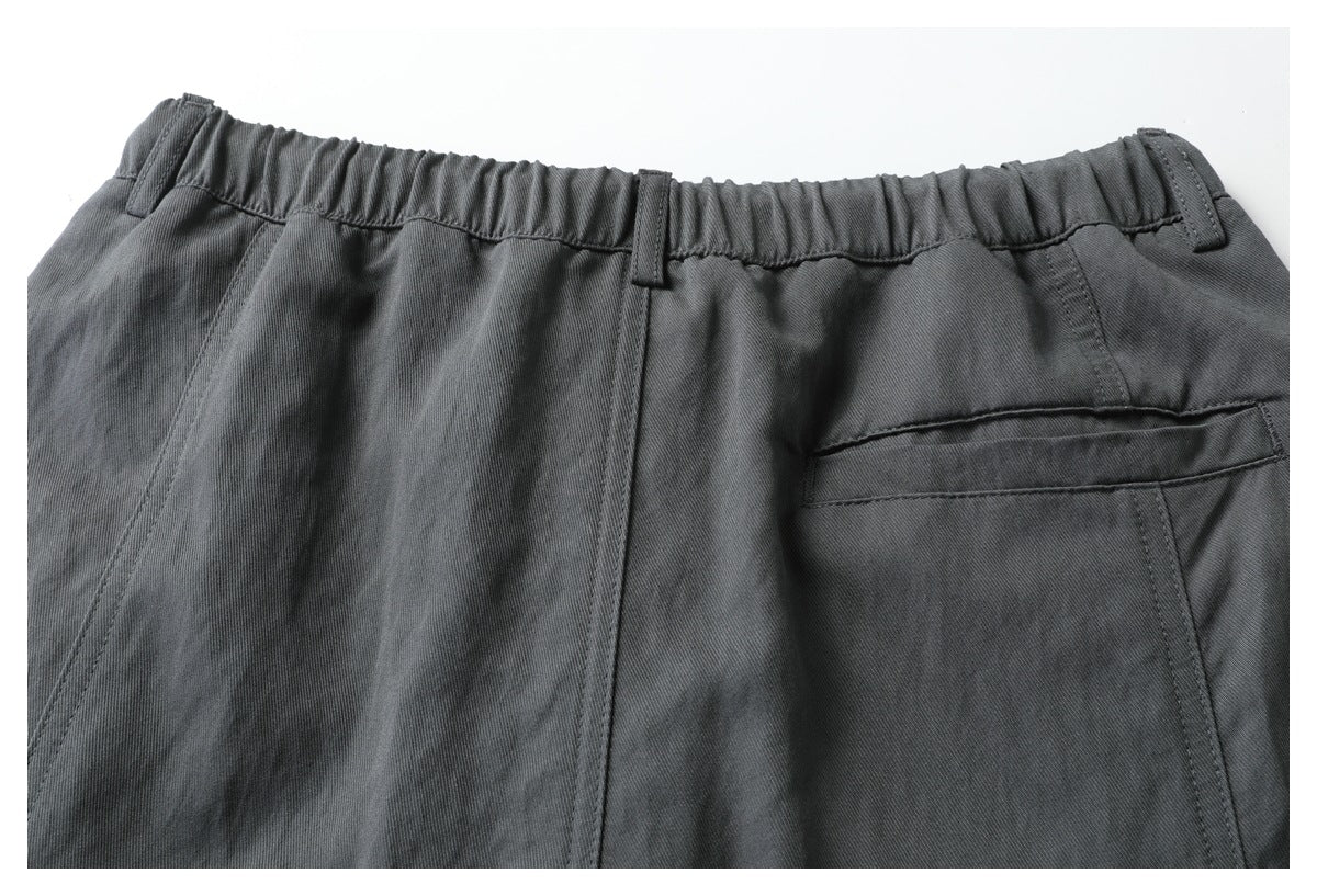 Close-up of the back upper section of charcoal trousers, showing an elastic waistband, belt loops, and a rear pocket.
