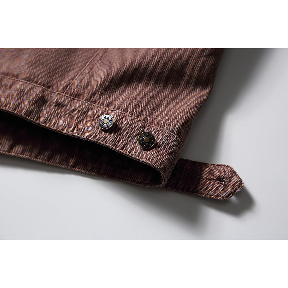 Close-up of a mauve-brown jacket cuff with two decorative metal snaps and an adjustable tab.