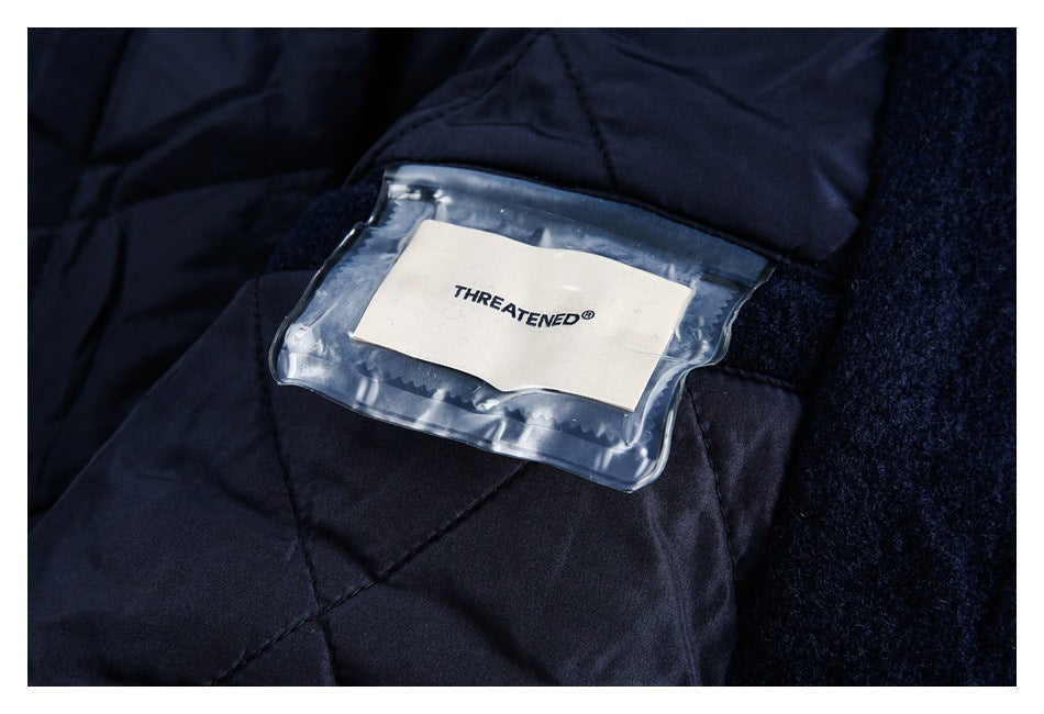 Close-up of dark navy quilted fabric with a clear pocket holding a white THREATENED label.