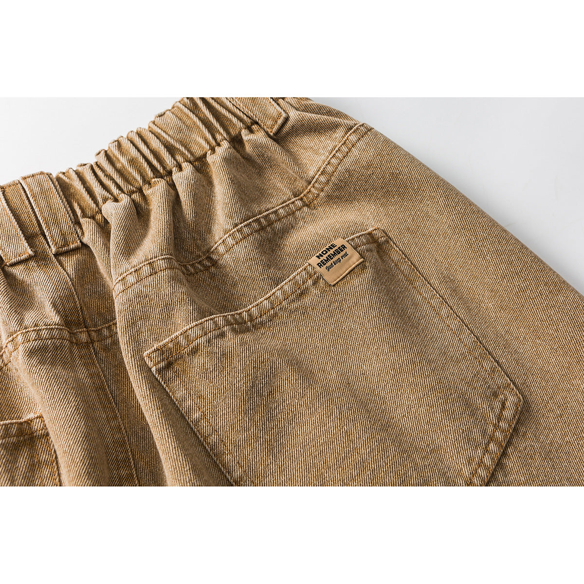 Close-up of the back waistband and patch pocket on tan washed jeans.