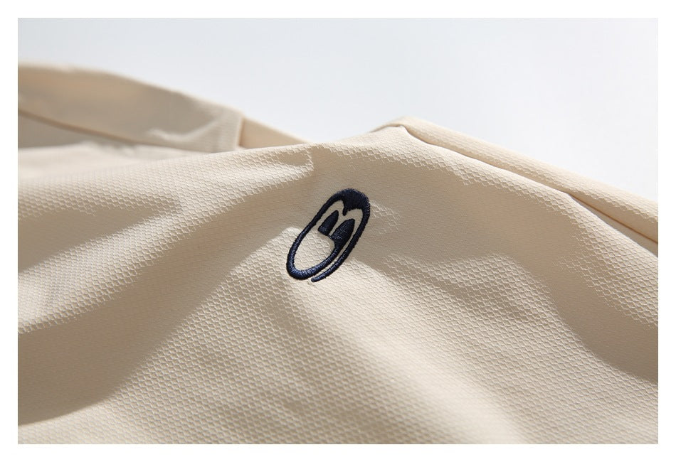 Close-up of a small dark embroidered emblem on textured cream fabric.