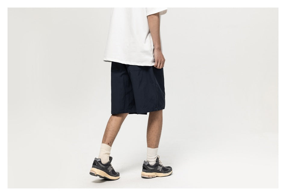 Cropped rear view of a model wearing dark navy knee-length shorts, a white T-shirt, and sneakers.