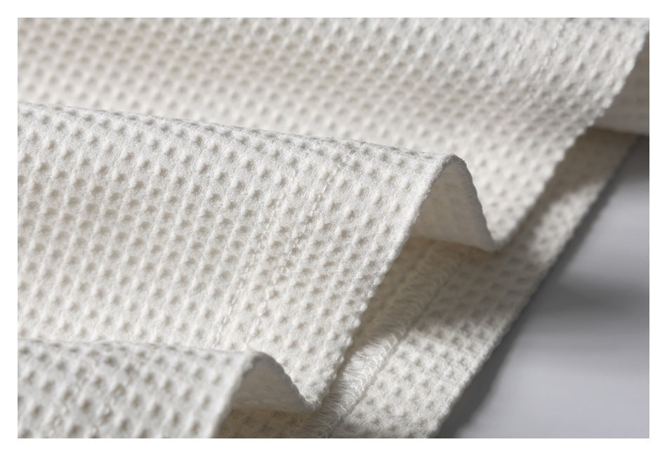 Close-up of the ivory waffle-knit garment's folded hem and stitched edge.