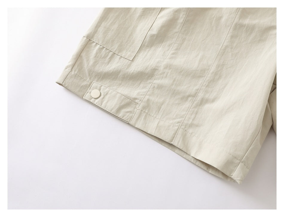Close-up of a cream garment's lower panel with a snap-button tab and visible seams.