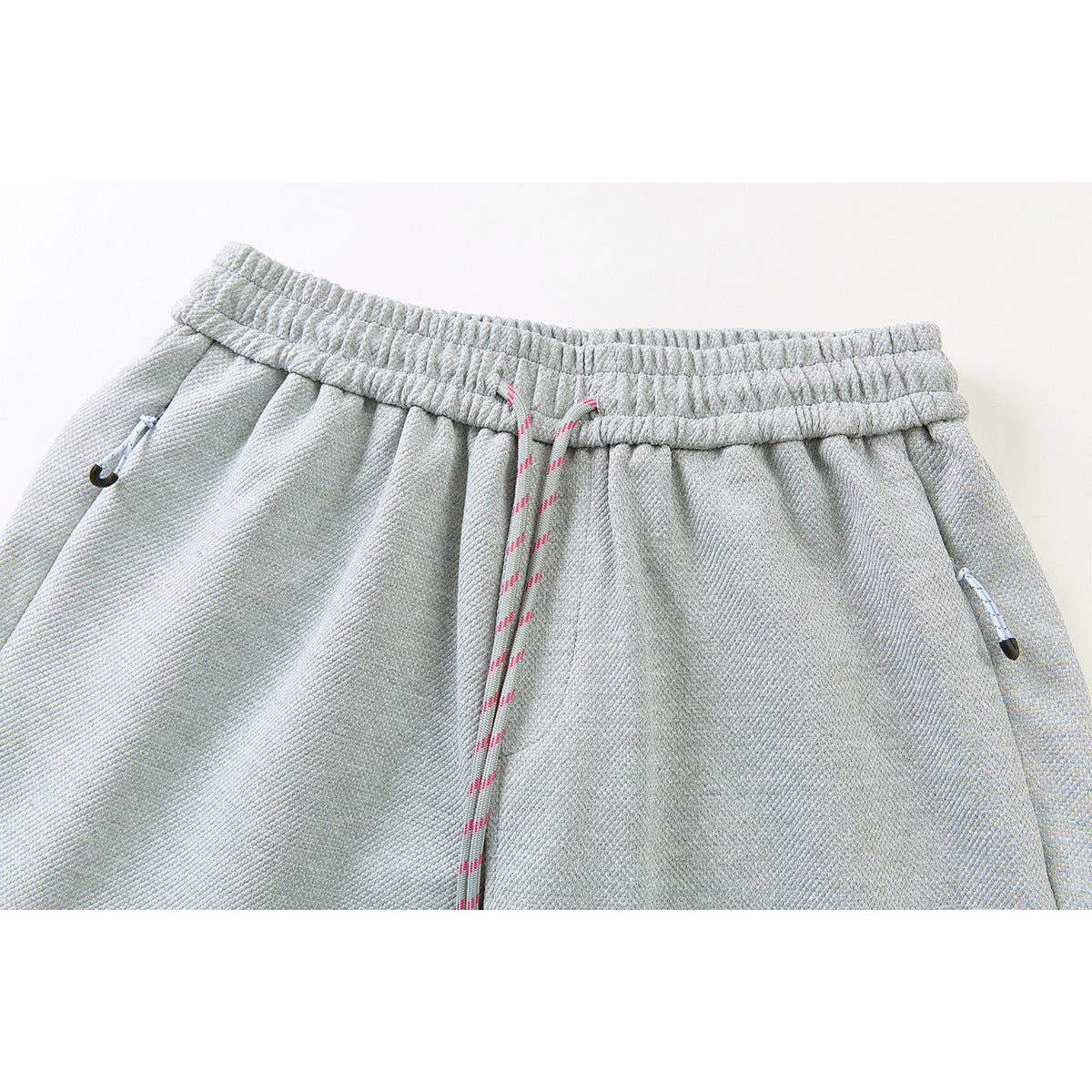 Close-up of light gray pants with an elastic waistband, pink-accented drawstring, and zippered pockets.