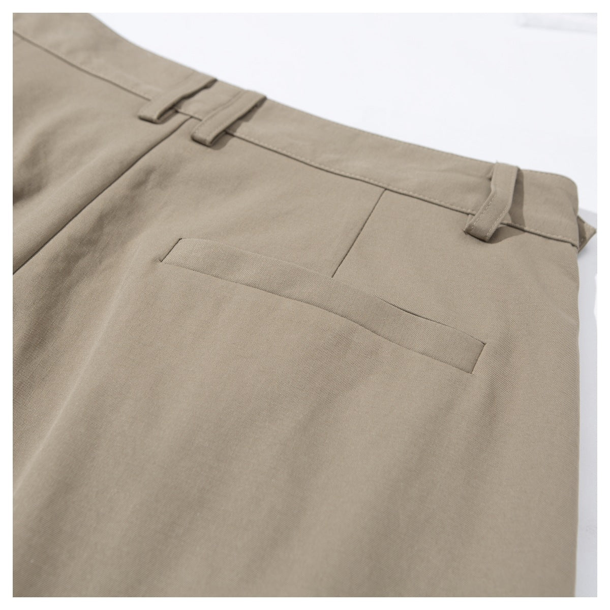 Close-up of taupe trousers showing a rear welt pocket, waistband and belt loops.