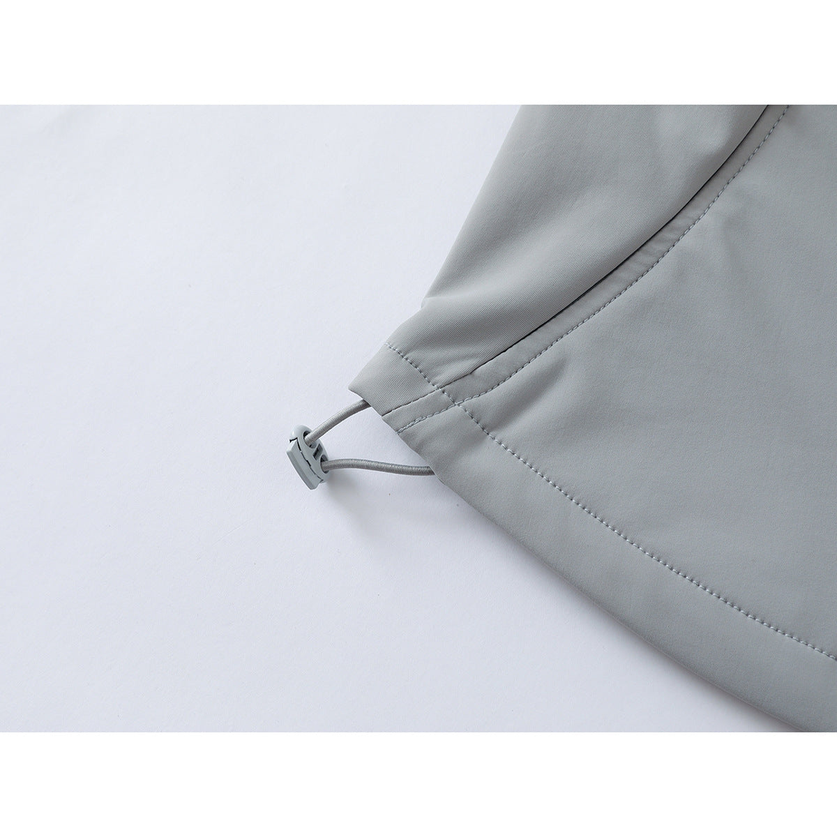 Close-up of a light gray jacket hem with an adjustable elastic drawcord and toggle.