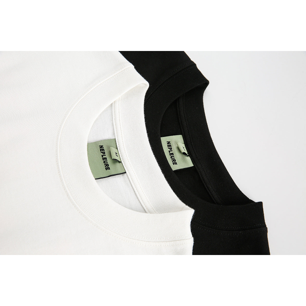 Close-up of white and black T-shirt ribbed crew necks with sewn-in green brand and size labels.