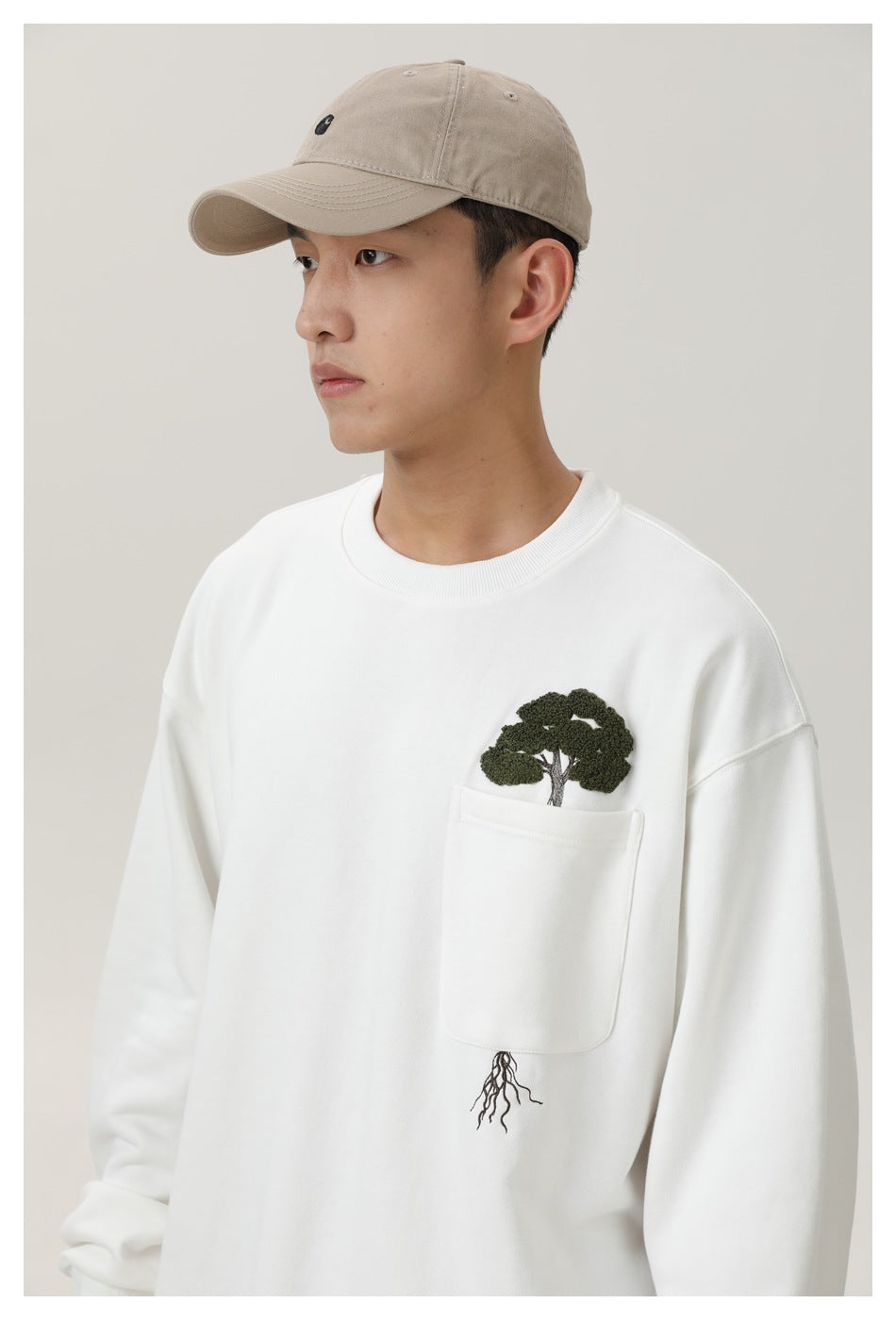 Close view of a model wearing a white sweatshirt with a pocket and embroidered tree-and-roots design.