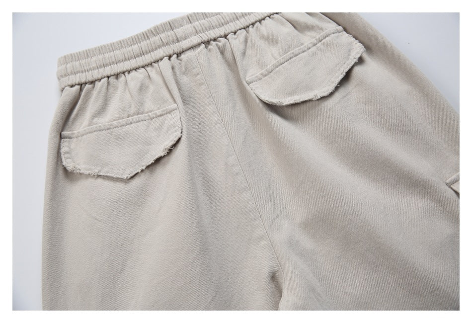 Close-up of beige trousers' elastic waistband and two rounded flap pockets at the back.