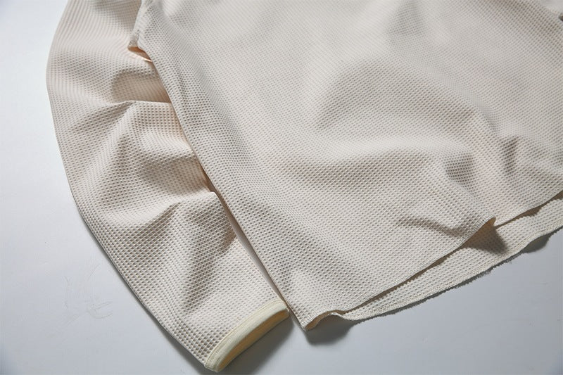 Close-up of a light cream garment showing its textured mesh fabric, sleeve cuff, and hem.