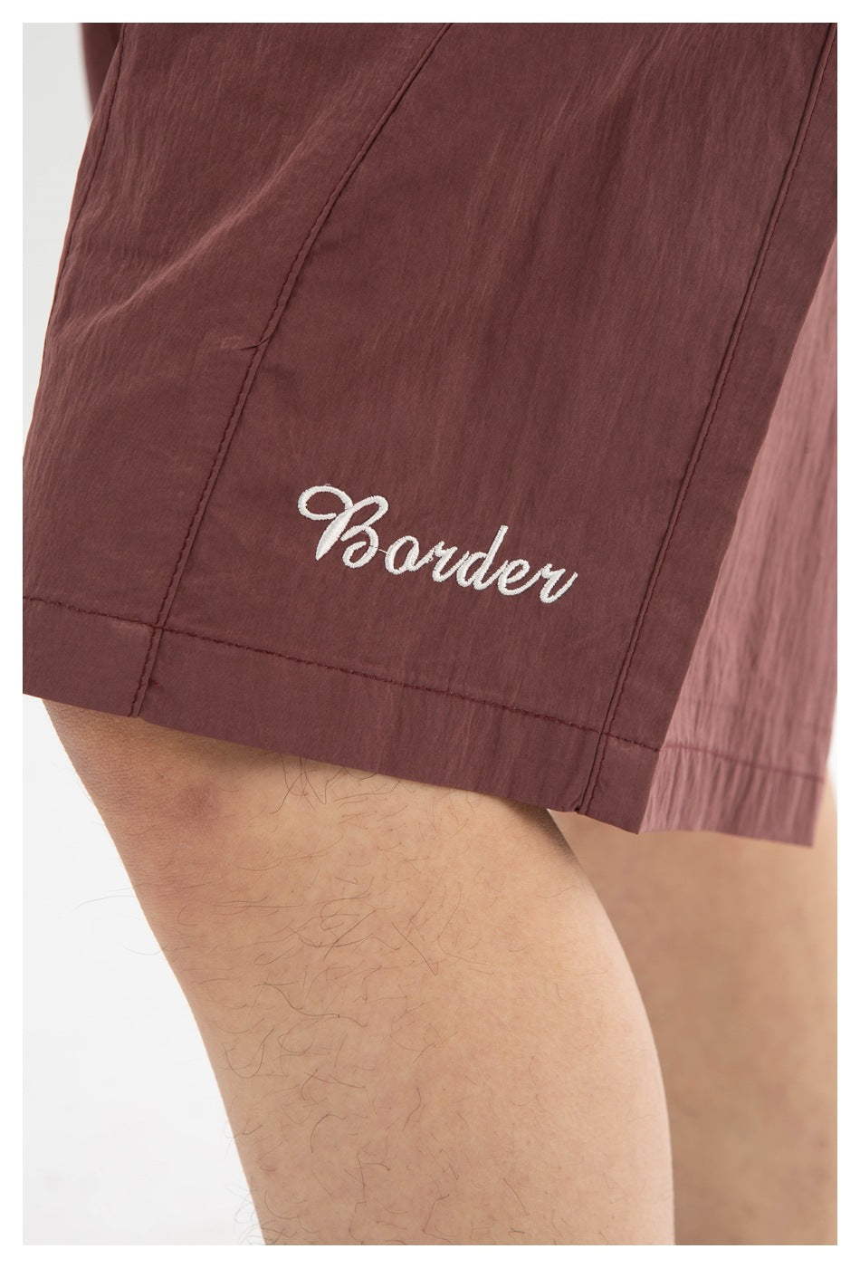 Close-up of white script embroidery and stitched seams on mauve shorts.