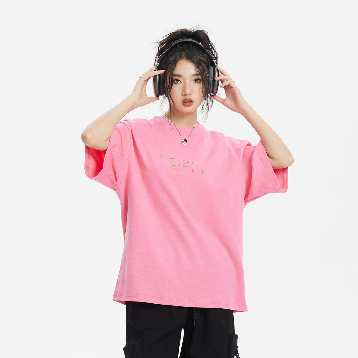 Model wearing an oversized bright pink T-shirt with small green chest lettering and black cargo pants.