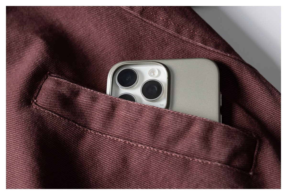 A smartphone peeks out of a stitched pocket on burgundy fabric.