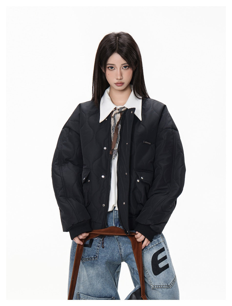 Closer front view of a model wearing a black quilted bomber jacket with ribbed cuffs and snap-fastened flap pockets.