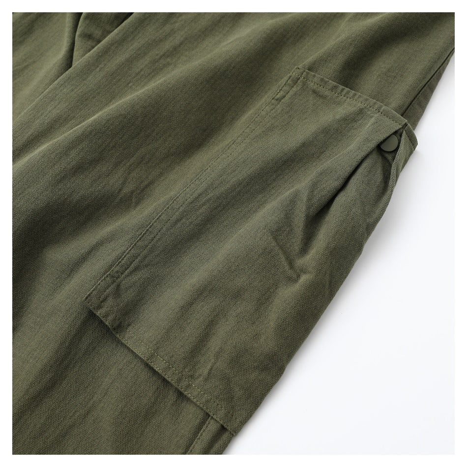 Close-up of olive-green trousers showing a stitched flap pocket with a dark snap button.