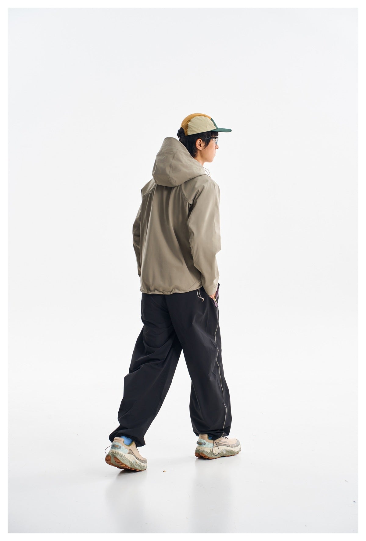 Rear view of a model wearing a light gray-beige hooded jacket and loose dark pants.