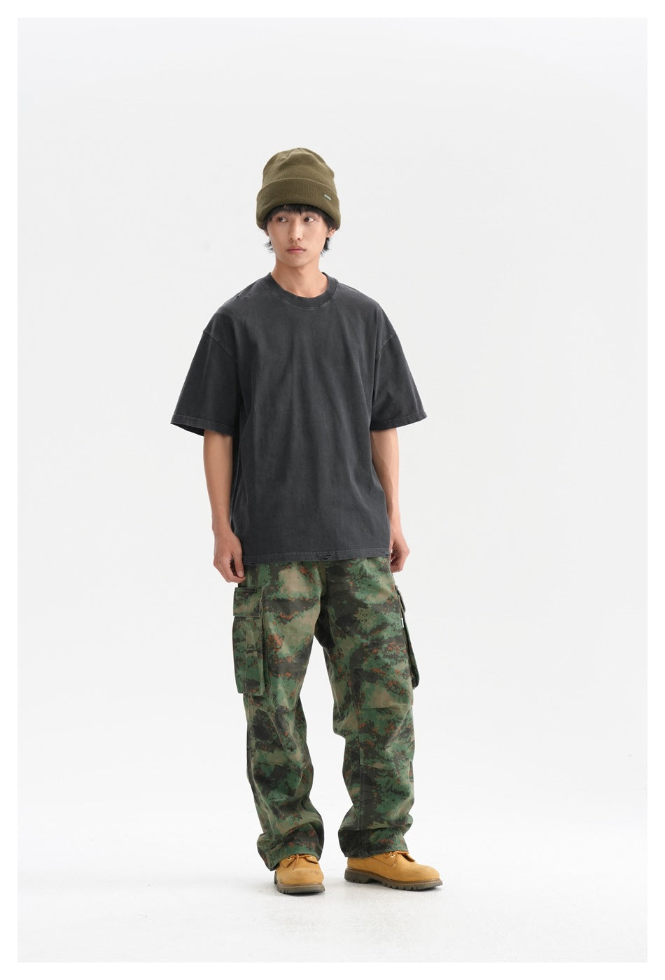 Model wearing an oversized charcoal T-shirt, green camouflage cargo pants, and an olive beanie.