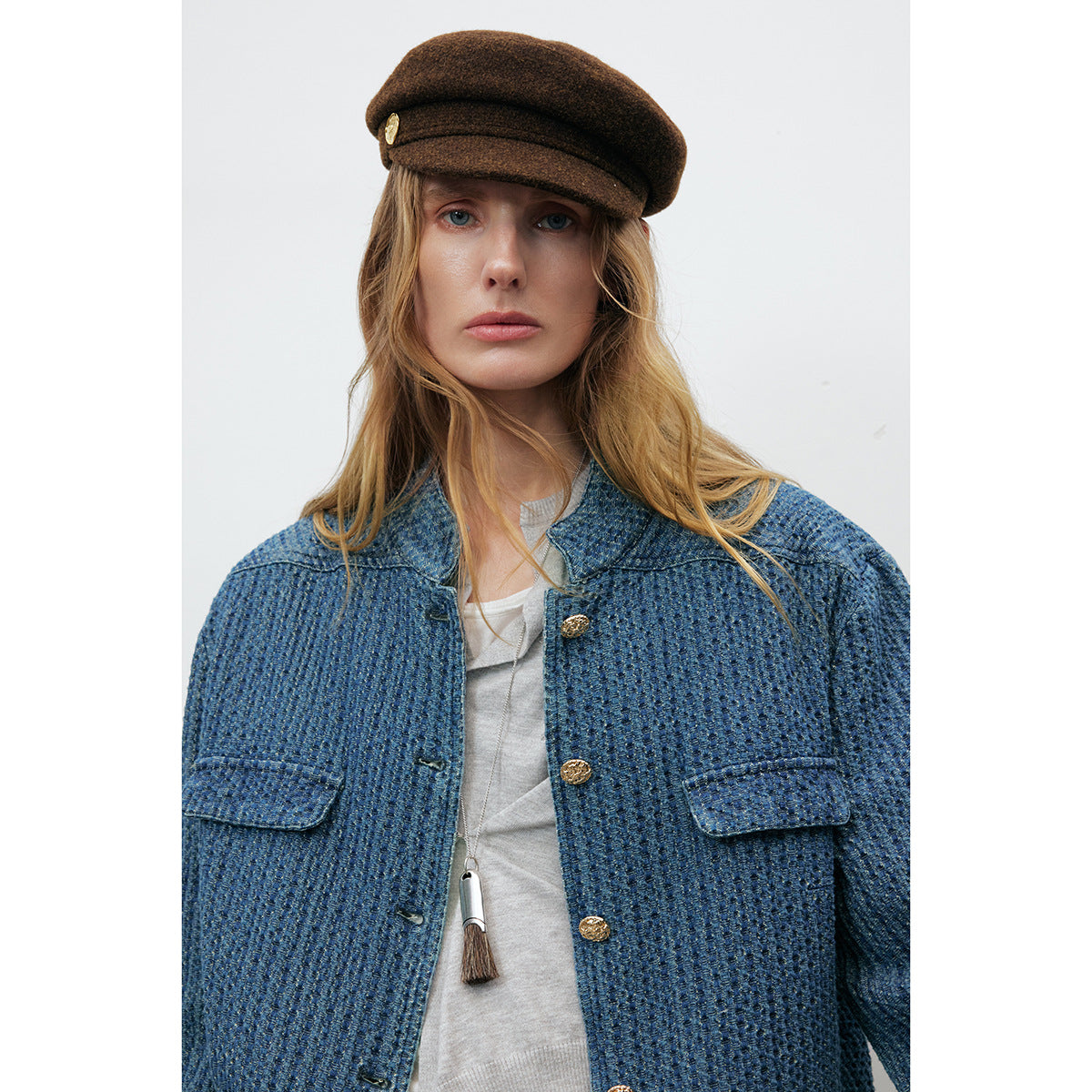 Close view of a model wearing a textured blue jacket with gold buttons and flap pockets over a white top.