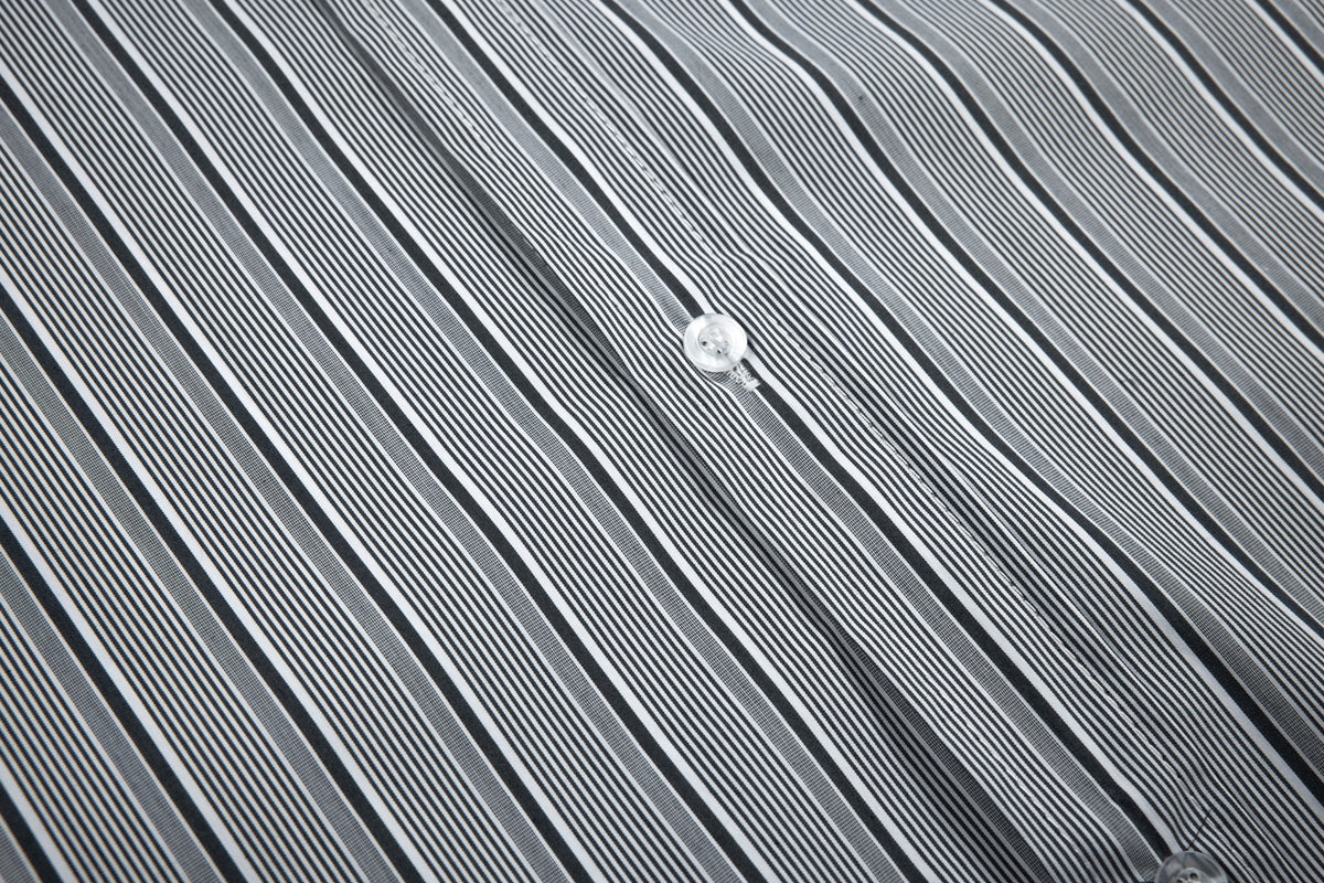 Close-up of a white button and placket on a black, gray, and white vertically striped shirt.