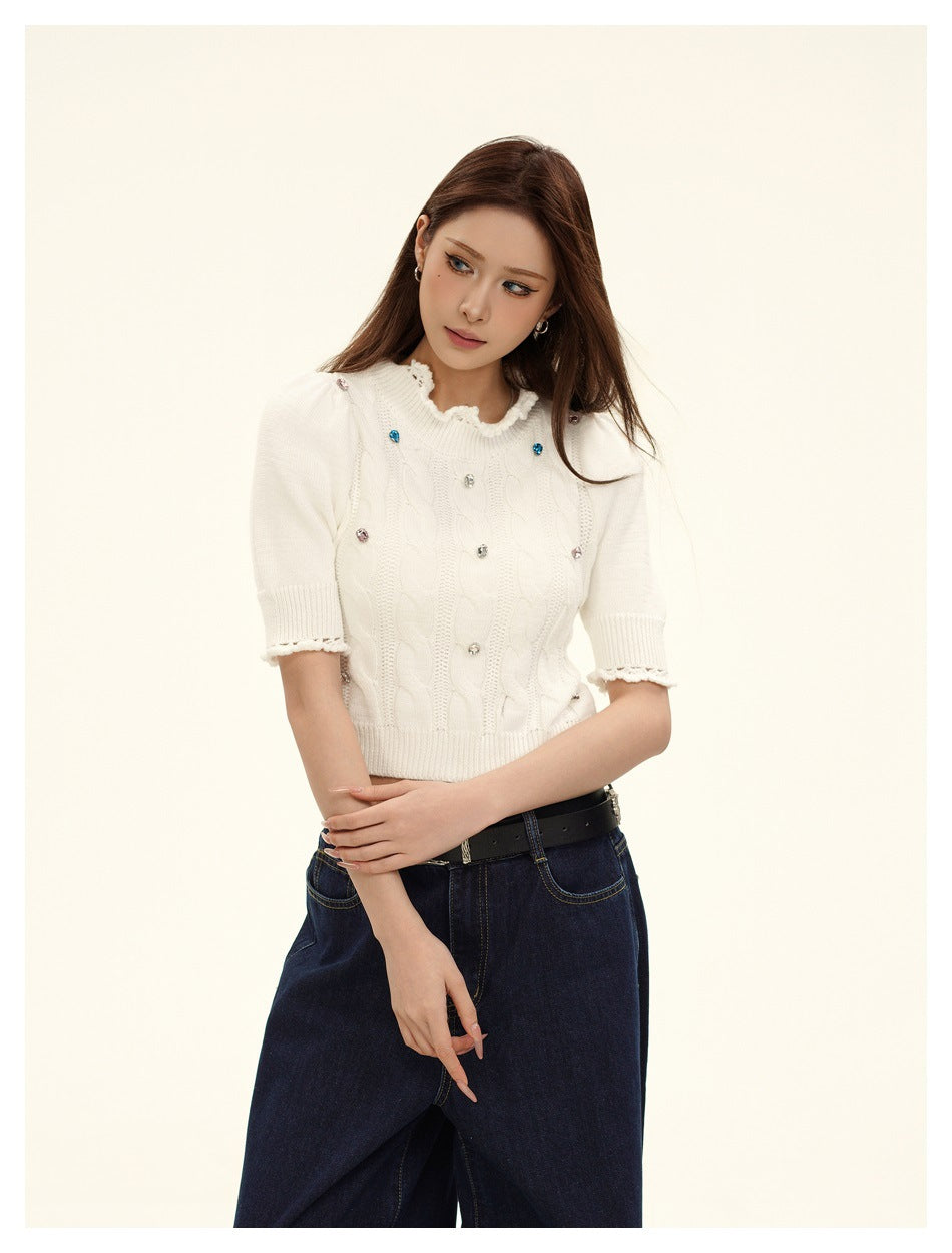 Model wearing an ivory embellished cable-knit top with puff sleeves and scalloped trim, paired with dark jeans.