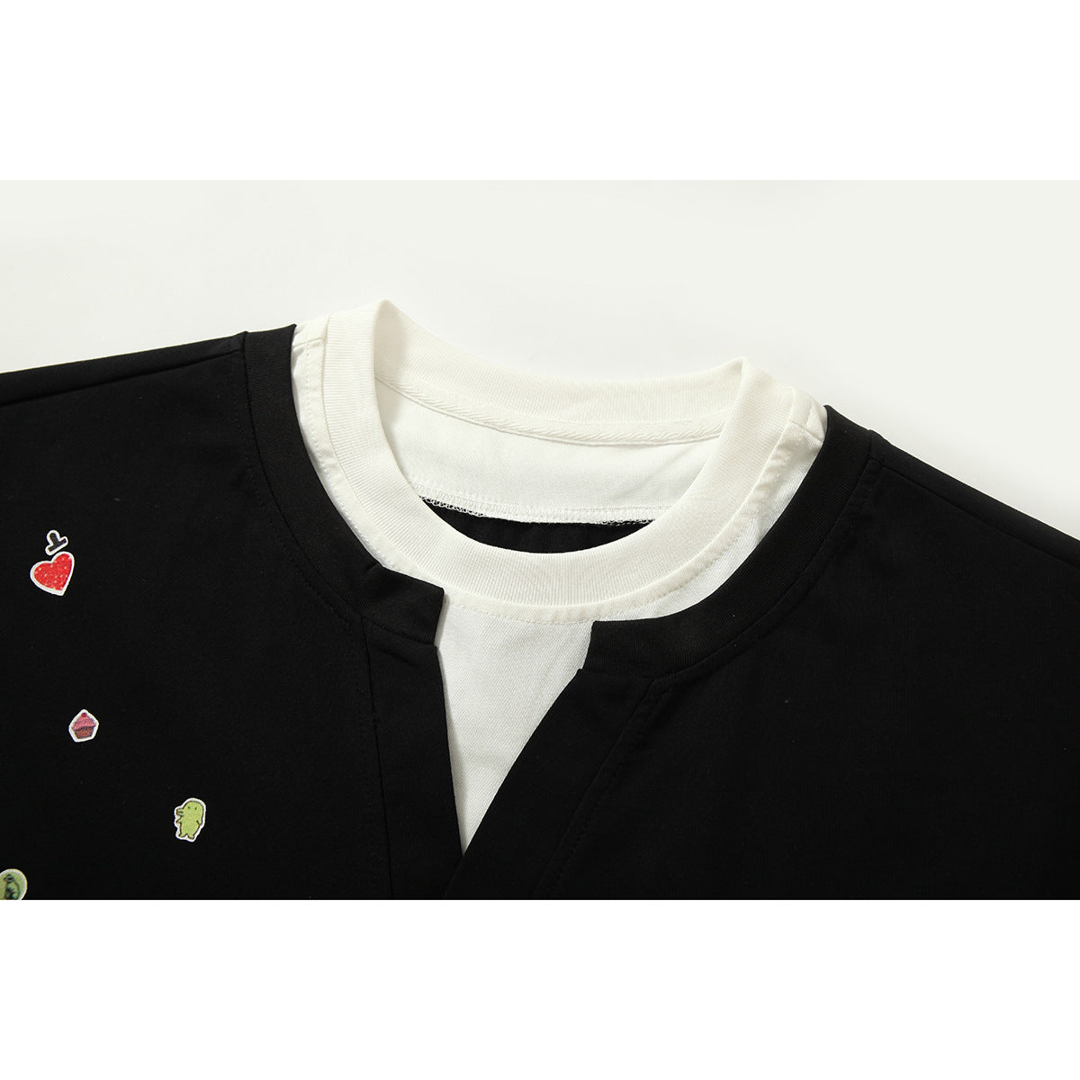 Close-up of a black T-shirt's layered white crew neck and V-notch, with small colorful motifs on the chest.