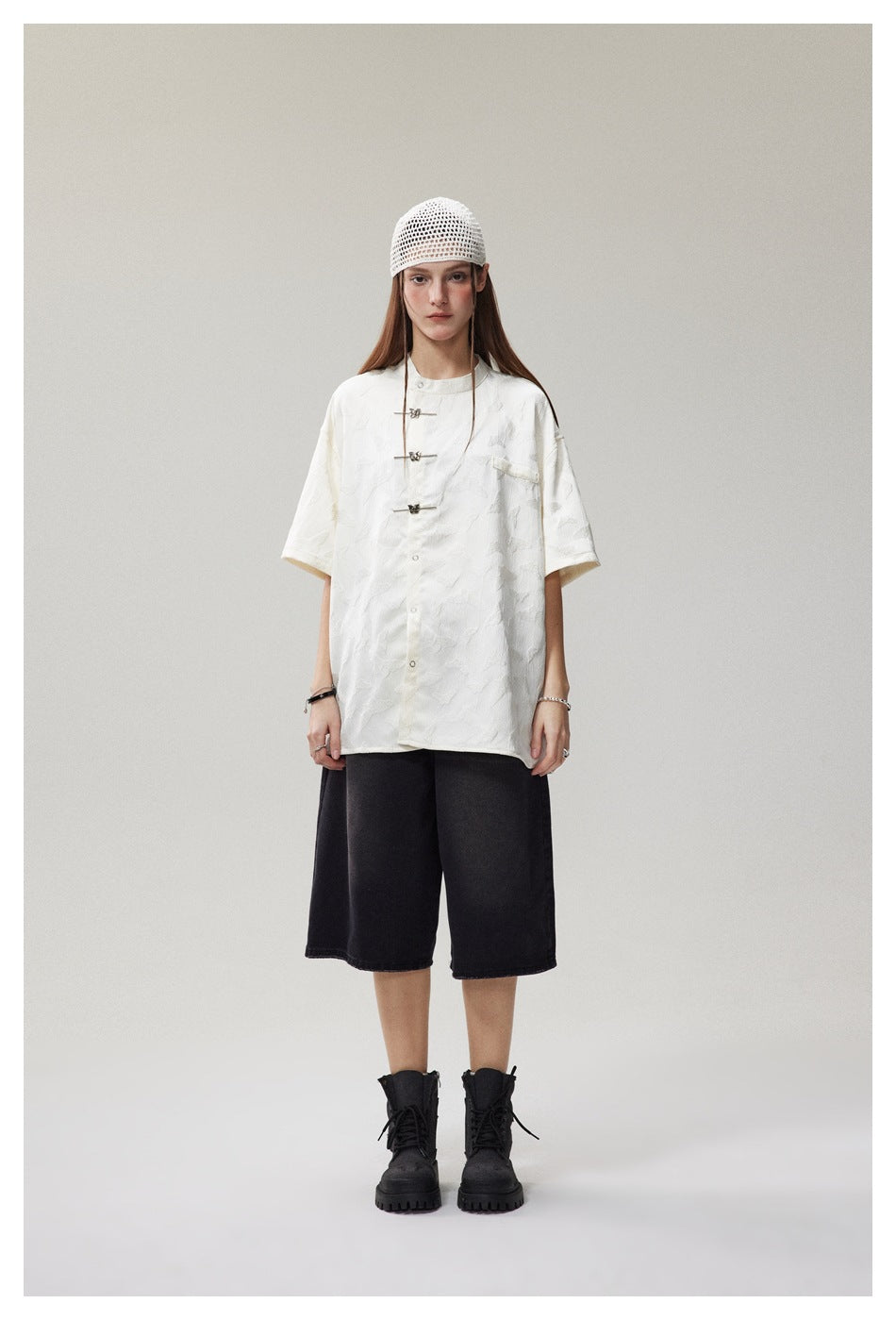 Model wearing an oversized white patterned short-sleeve shirt with frog closures, black knee-length shorts and a white