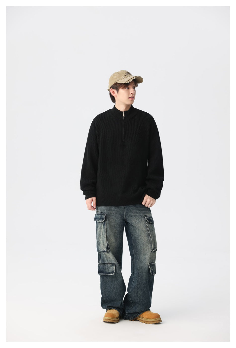 Model wearing a black ribbed quarter-zip sweater with faded cargo jeans, a tan cap and tan boots