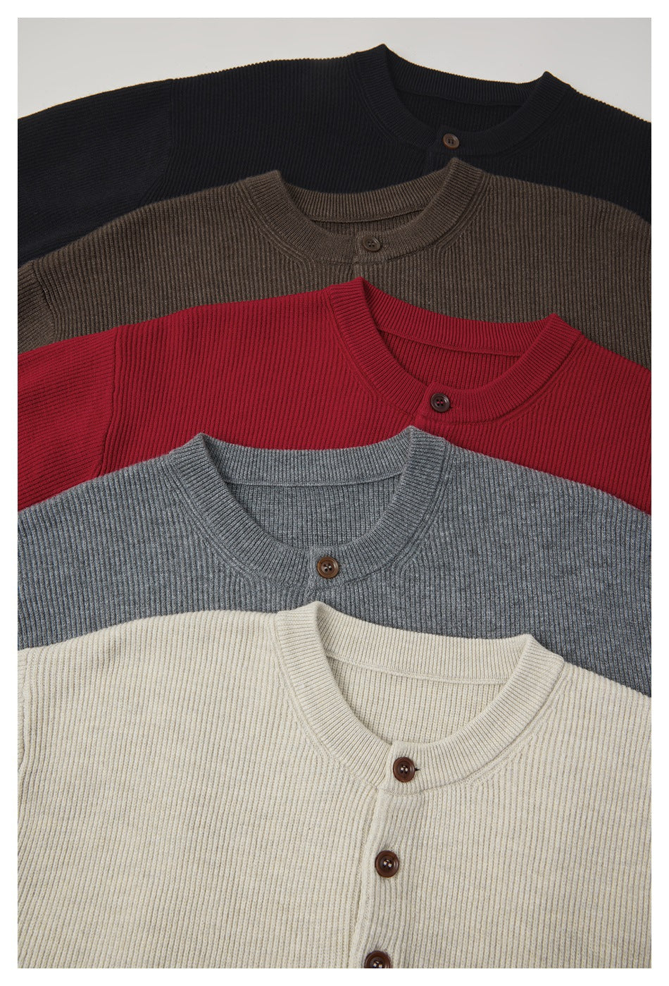 Close-up of rib-knit button-front sweaters in black, brown, red, gray, and cream, arranged in overlapping layers.