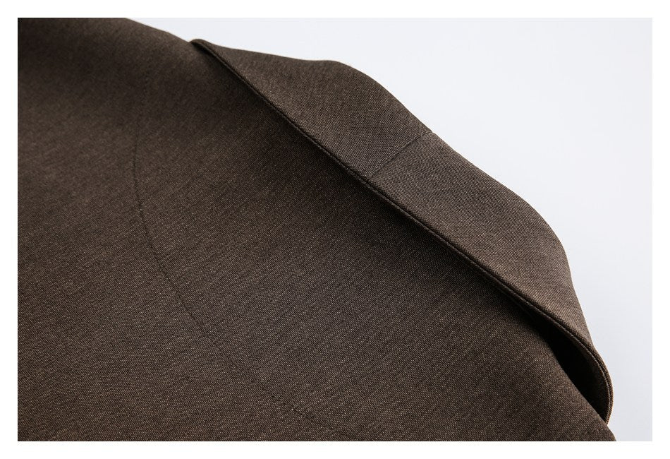 Close-up of a dark brown blazer shoulder and notched lapel against a pale background.