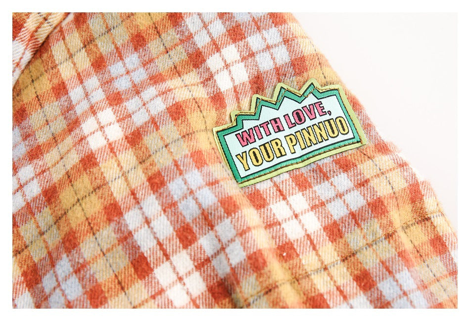Close-up of a colorful text appliqué on the sleeve of the plaid jacket.