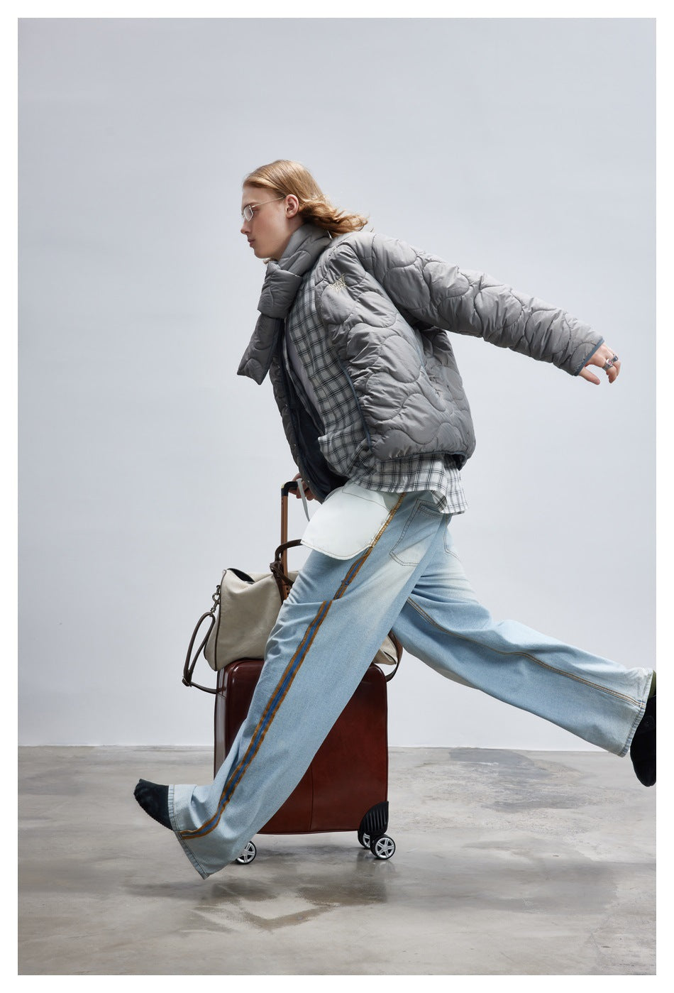 Side view of a model in a gray wave-quilted jacket and scarf with wide light-blue jeans.