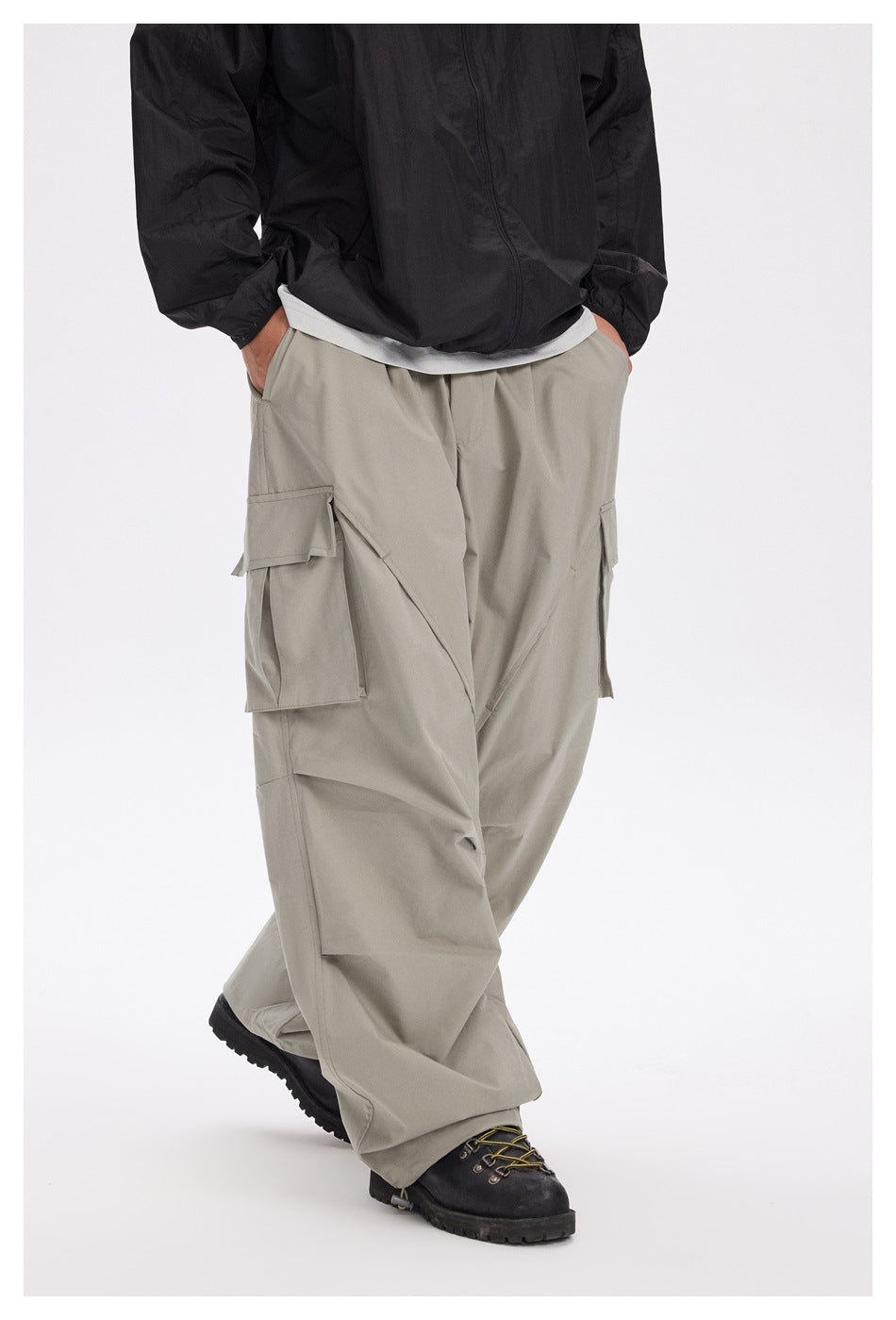 Model wearing loose light gray cargo pants with large flap pockets and angular panel seams, shown at a three-quarter angle.