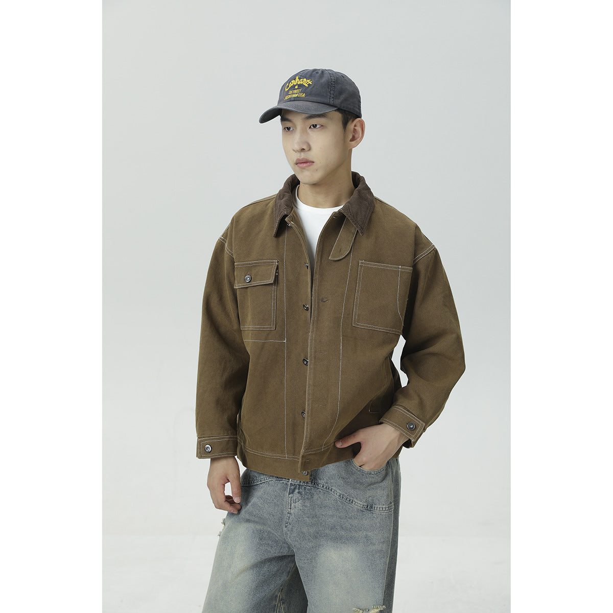 Front view of a model wearing a brown work jacket with a corduroy collar and contrasting stitched chest pockets.