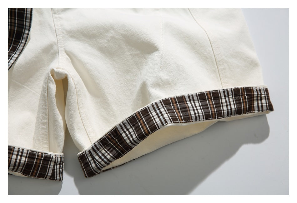 Close-up of ivory shorts with dark brown plaid trim along the turned-up leg hems.