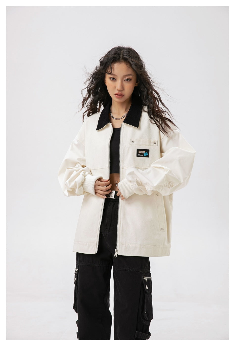 Front view of a model wearing an ivory zip jacket with a black collar and chest patch, paired with black cargo pants.
