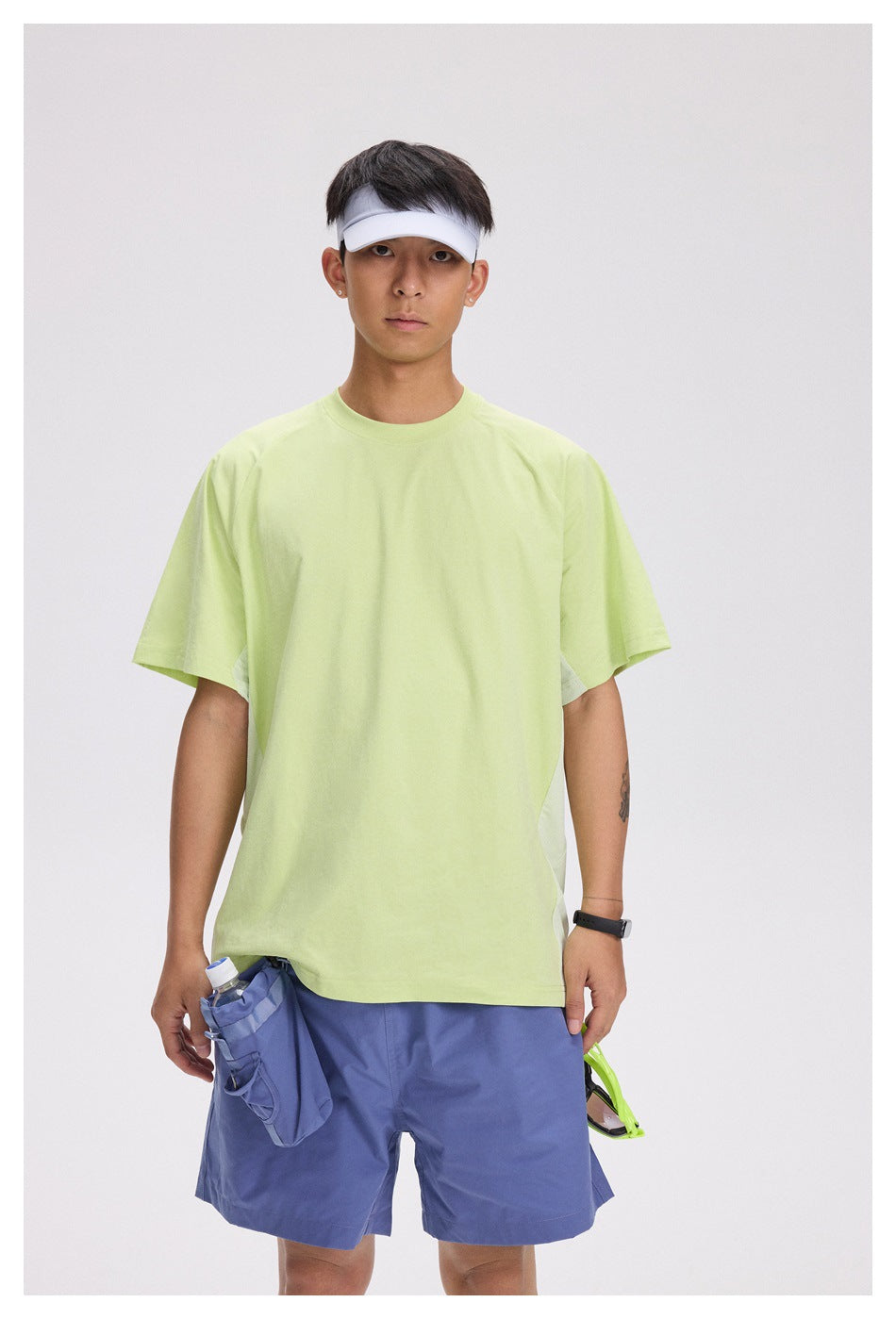 Model wearing a loose pale lime short-sleeve T-shirt with blue-purple shorts, shown from the front.